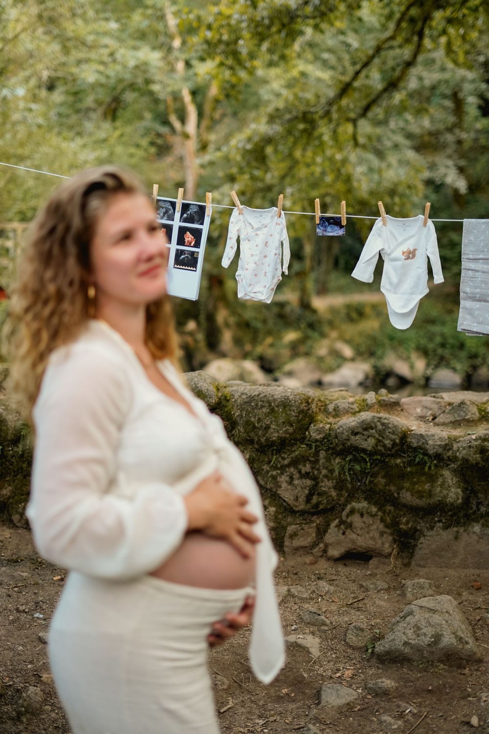 Baby clothes and ultrasound photos hung on clothesline with maternity figure in background.