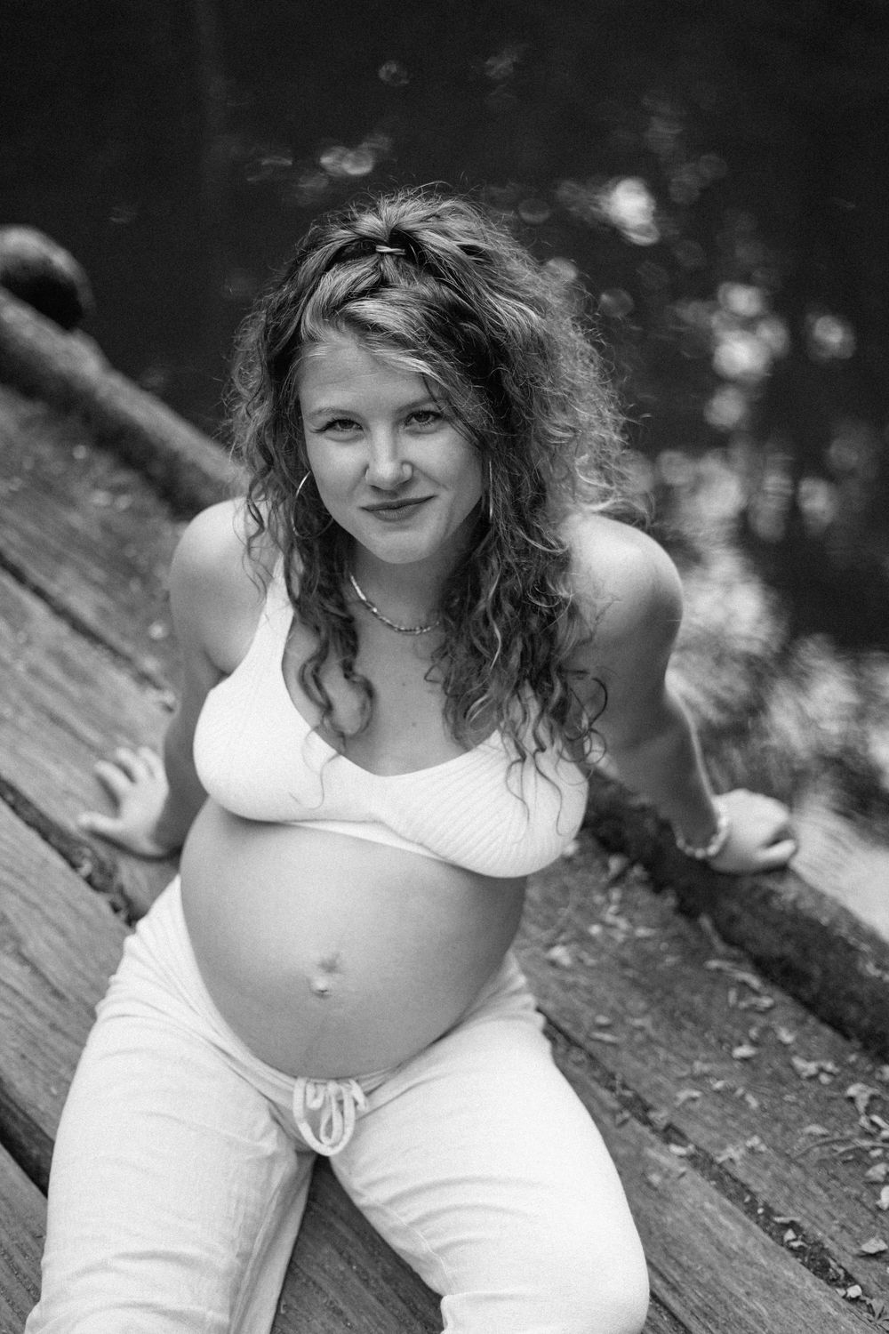 Black and white maternity portrait on rustic wooden surface in natural setting.
