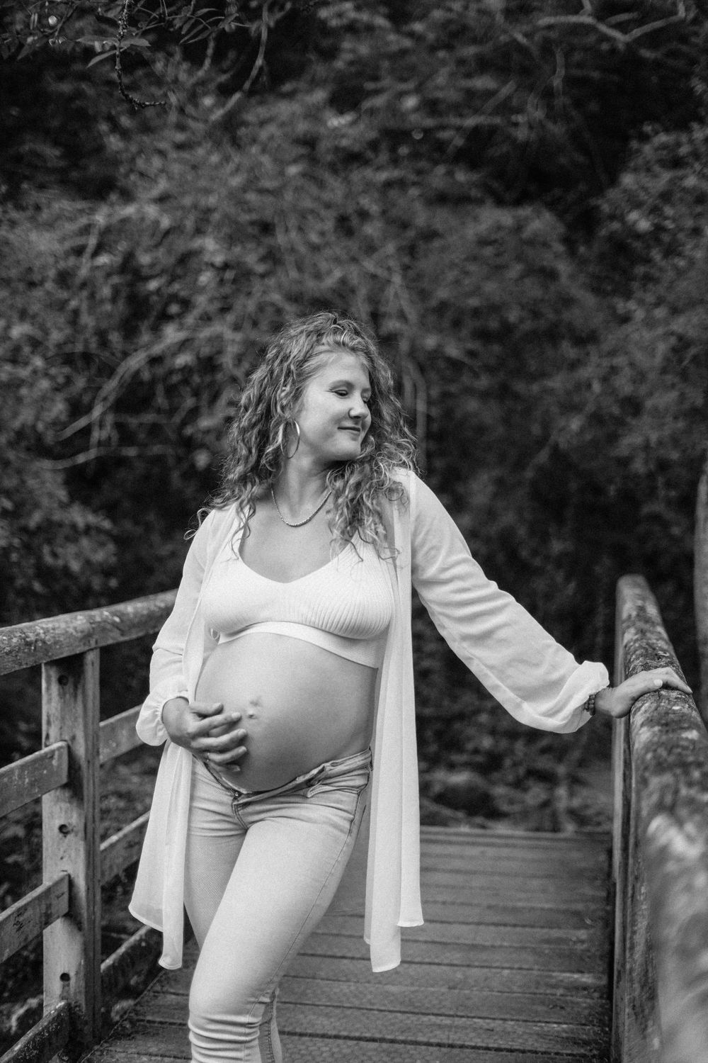 Black and white maternity photo on wooden bridge showing casual outdoor pose.