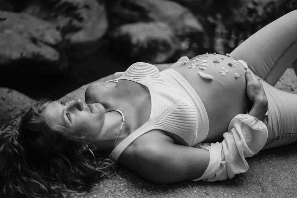 Artistic black and white maternity portrait showing expecting mother lying down with butterfly decorations.