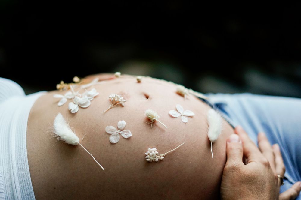 Creative maternity photo with small white flowers decorating pregnant belly against dark background.