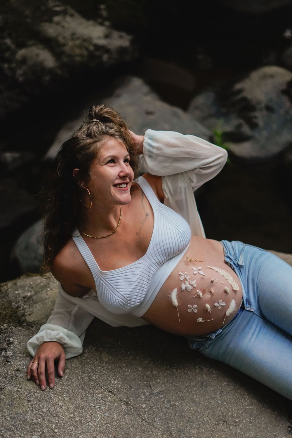 Artistic maternity photo with delicate white flowers arranged on pregnant belly outdoors.