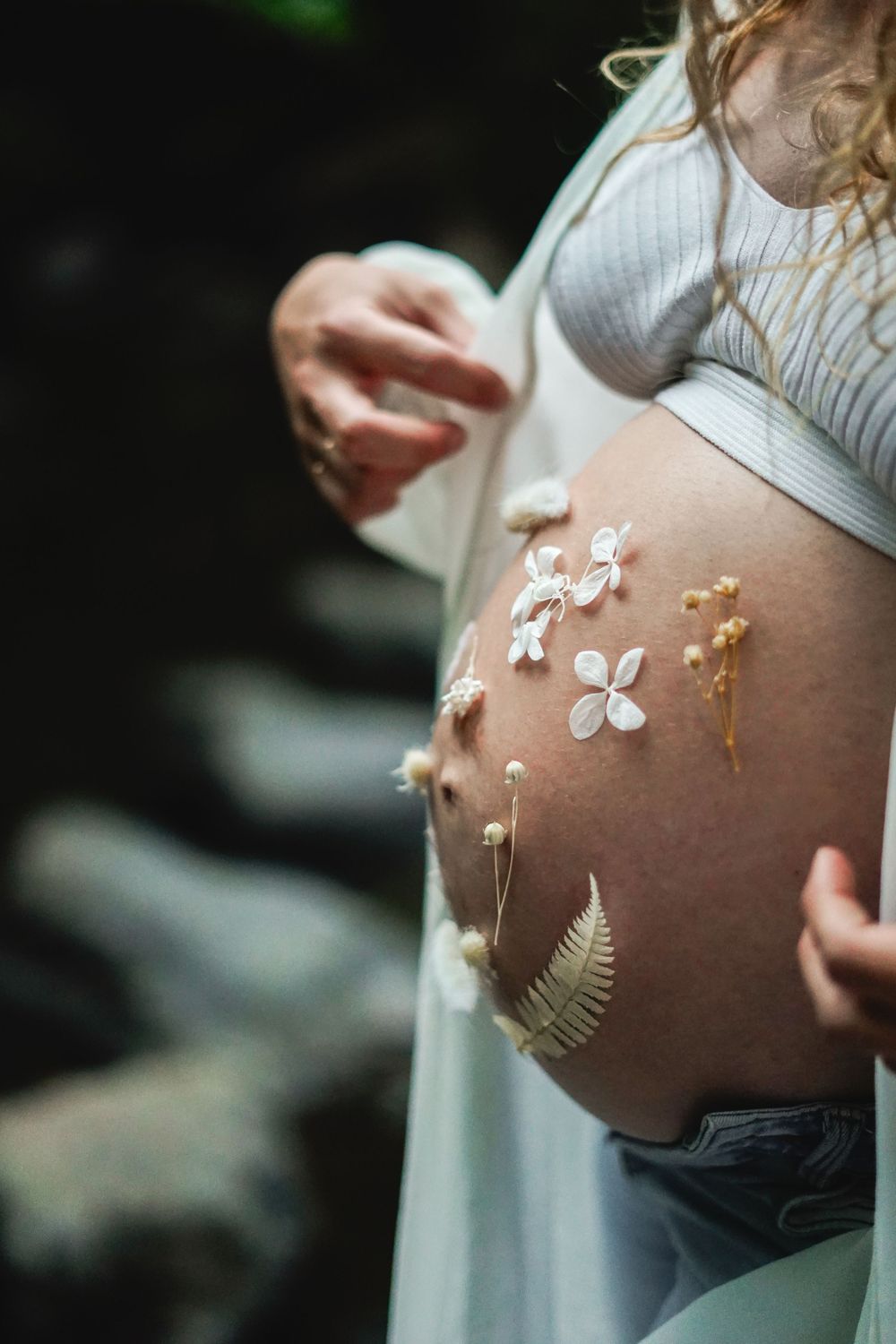 Detailed close-up of pregnant belly decorated with botanical elements and white flowers.