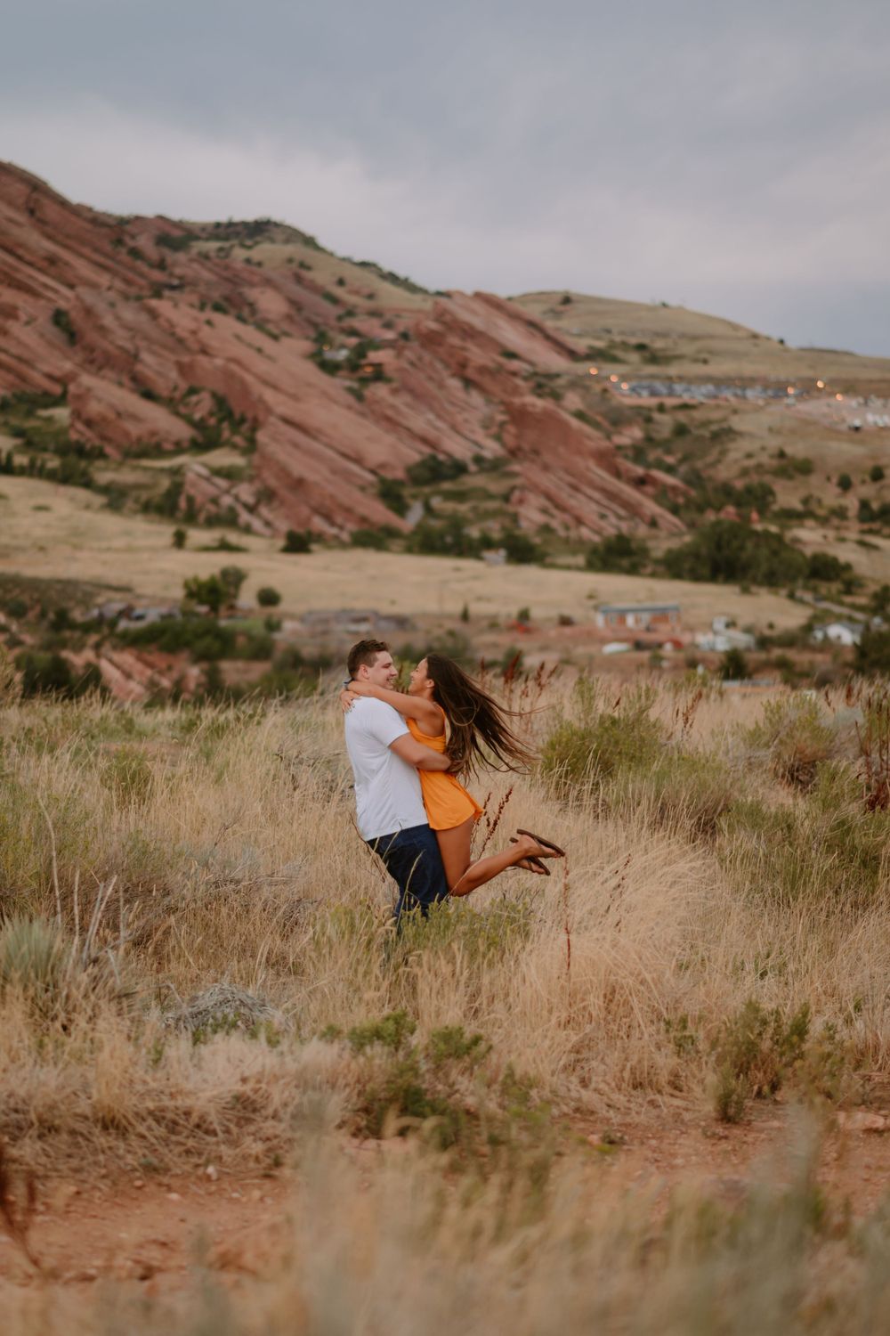A couple embraces in a field with red rock formations in the background.