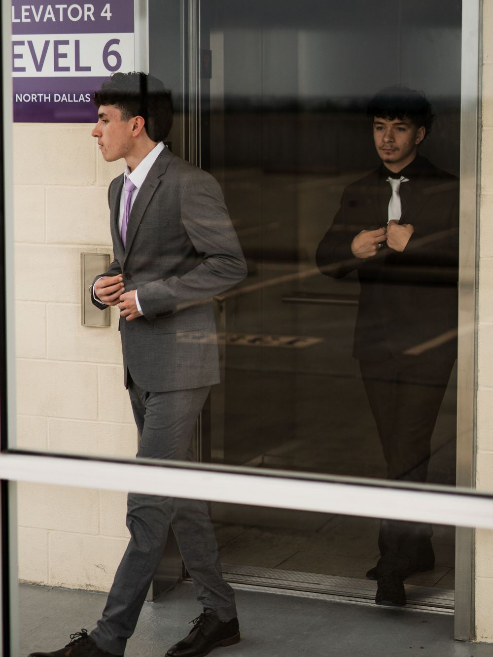 Person in formal attire standing by an elevator on Level 6 with their reflection visible.