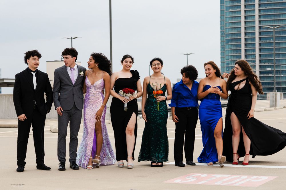 Group of friends posed together in formal attire on a rooftop with city buildings in background.