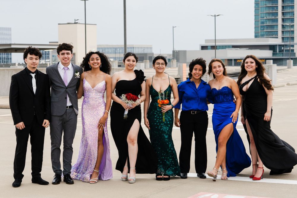 Group photo of friends in elegant formal wear standing together on urban rooftop.