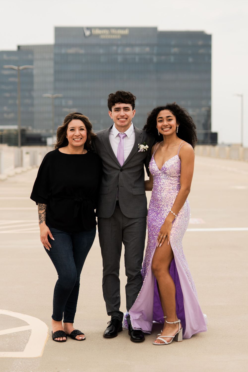 Three people pose together at prom, with one wearing a sparkly purple gown and another in a grey suit with purple tie.