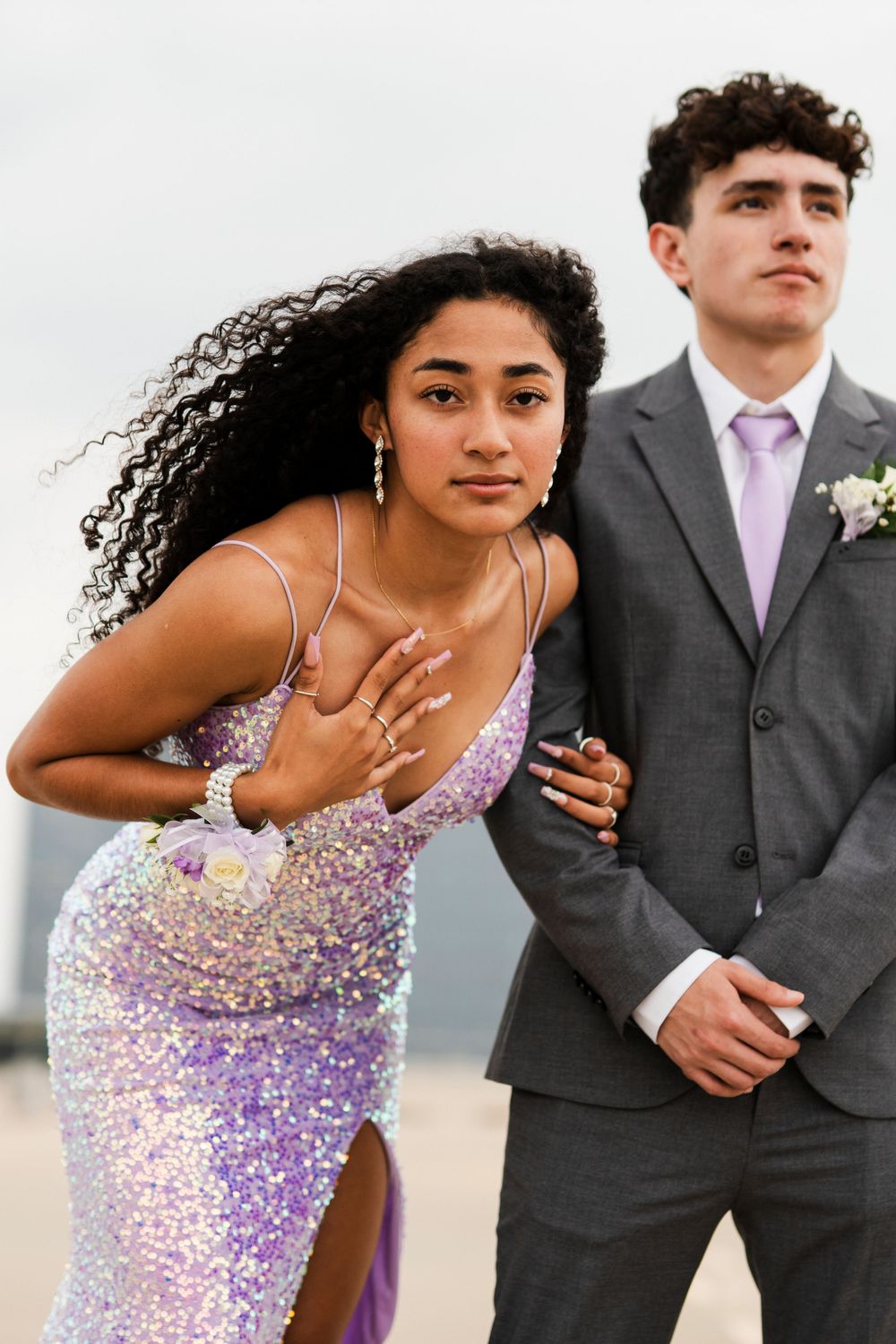 A couple poses together at prom, with one in a sequined purple dress showing their corsage.