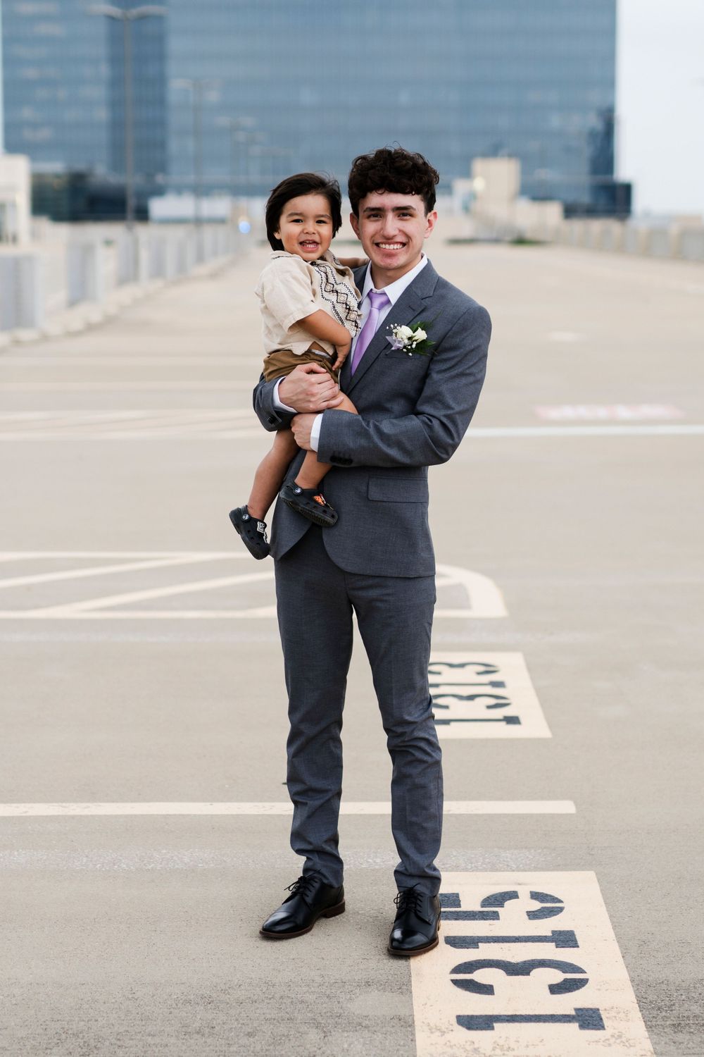 A person in a grey suit holds a small child while standing on a rooftop parking deck.