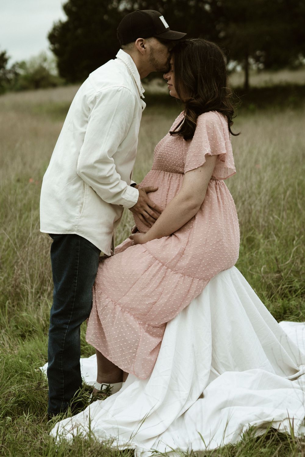 An intimate maternity moment captured on a white blanket in a rustic field setting.