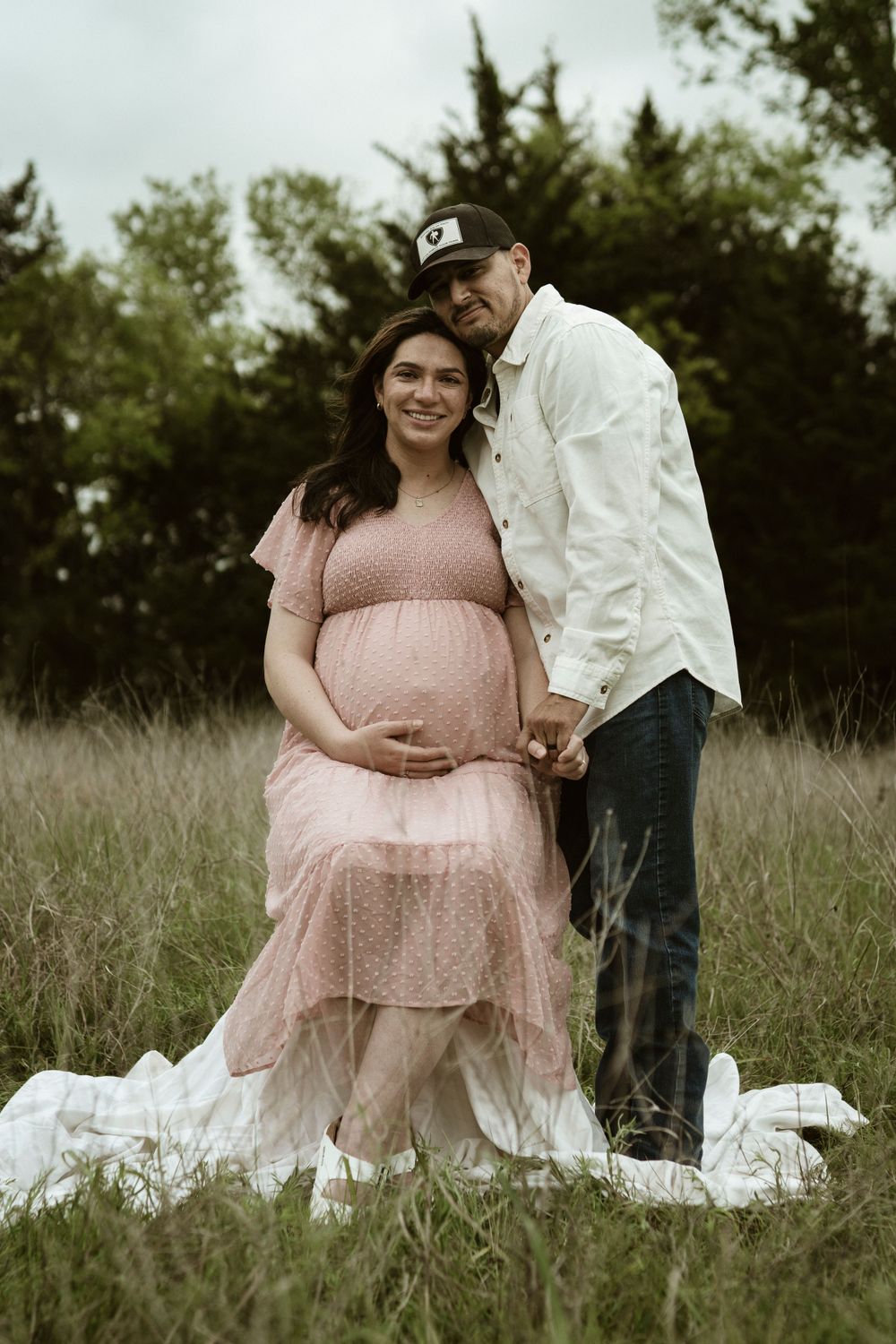 A romantic outdoor maternity photo featuring a couple in coordinated white and pink outfits.