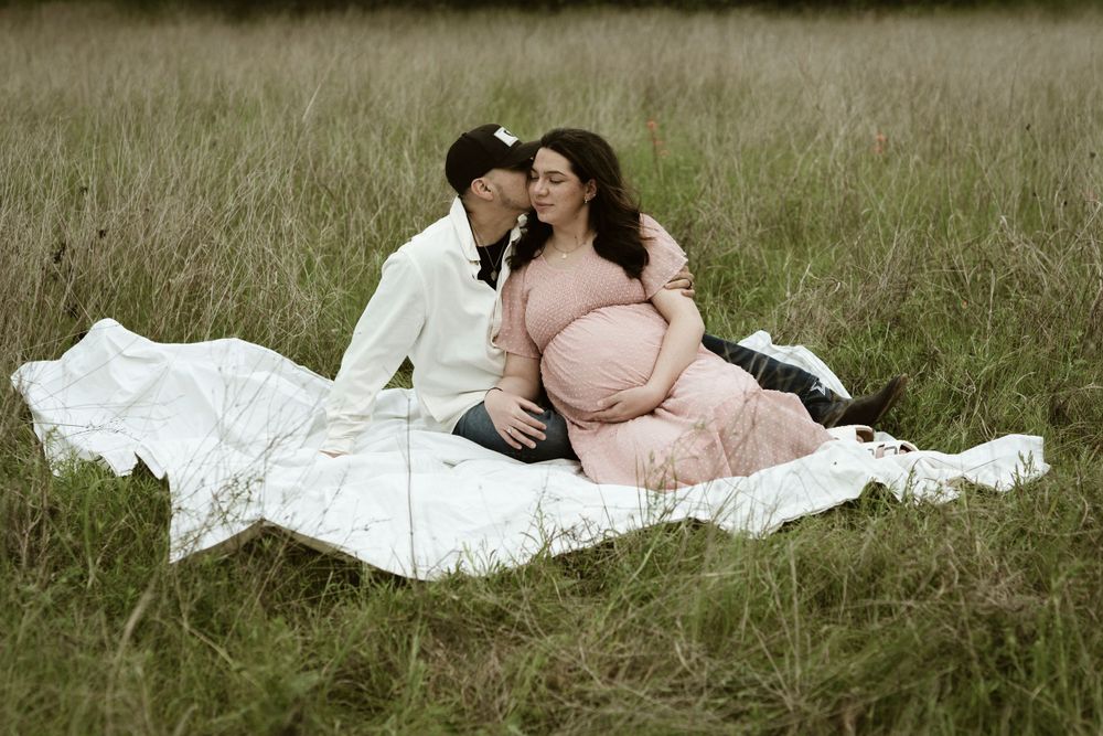 A sweet maternity photo of a couple relaxing on a white blanket in tall grass.