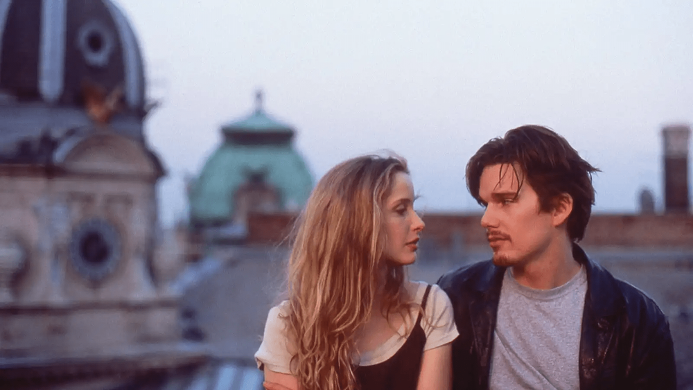 Two people in conversation at sunset against an urban rooftop backdrop.