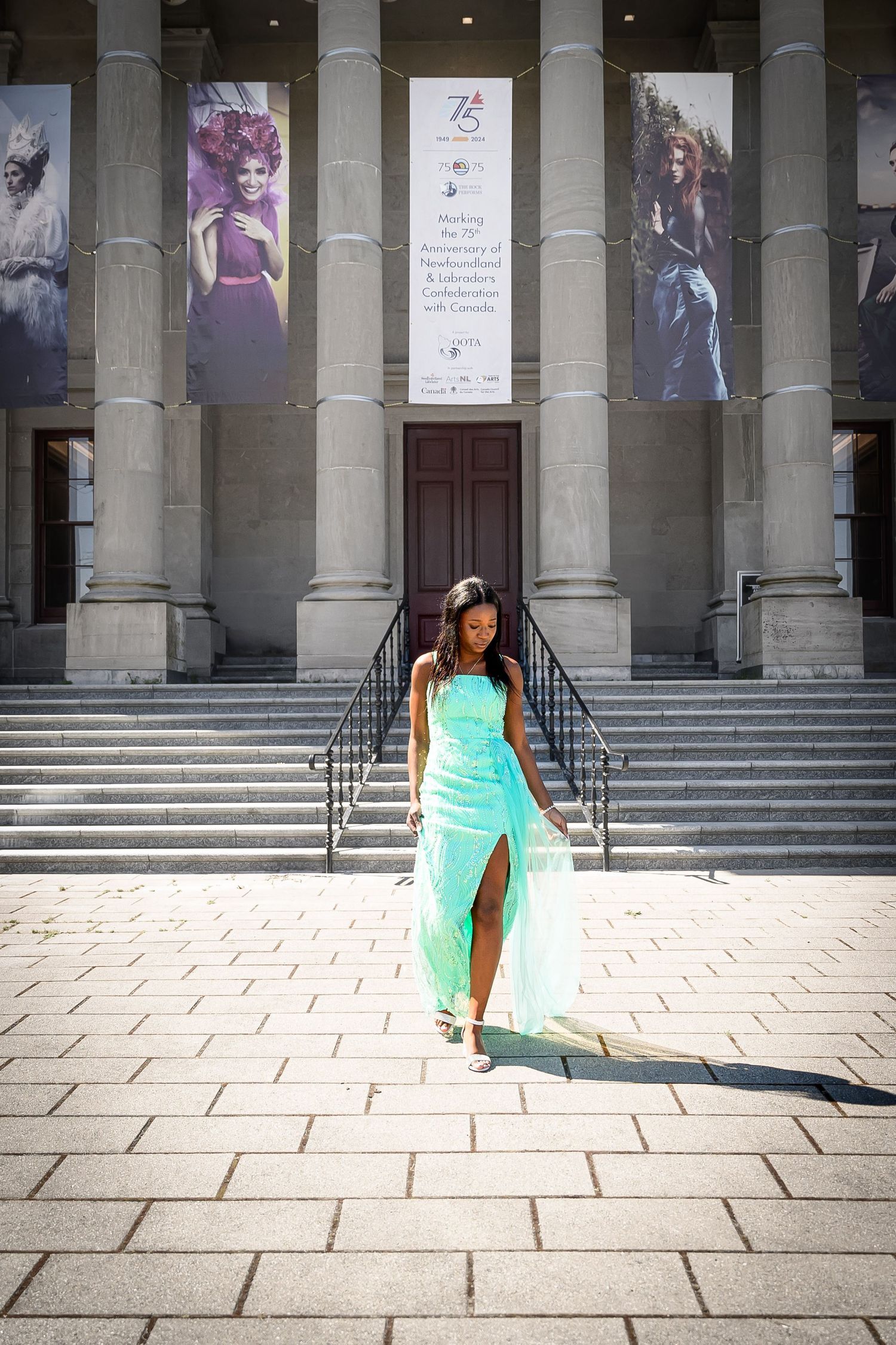 High school grad in a teal dress, her warm brown skin a striking contrast against the historic Colonial Building, St. John's, Newfoundland.