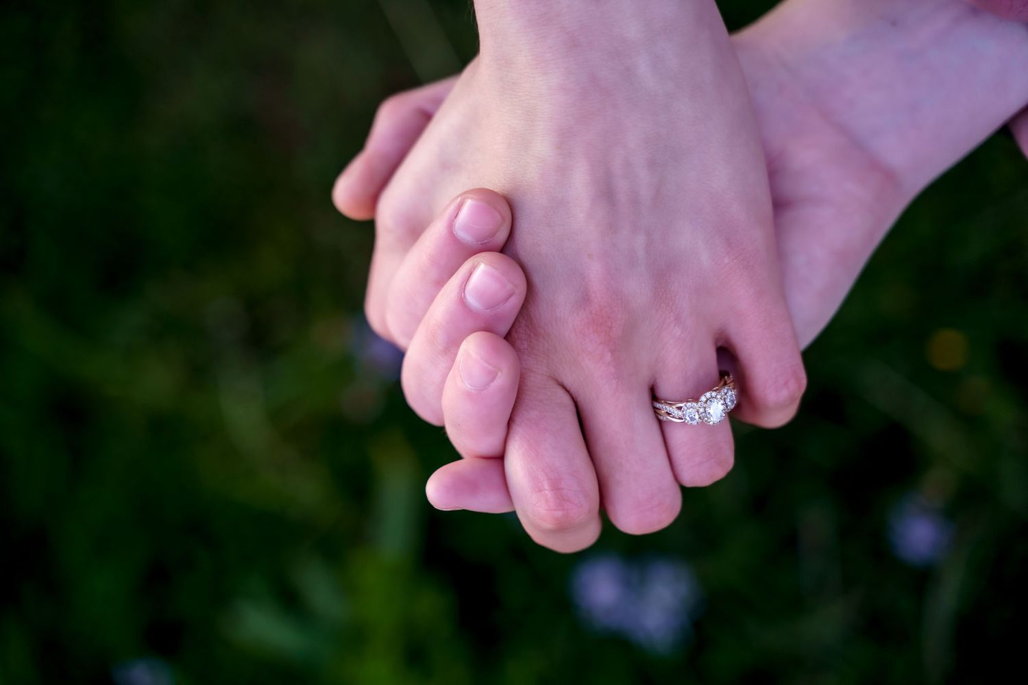 Newlyweds holding hands over green moss and wild brush, wedding rings just placed, Newfoundland.