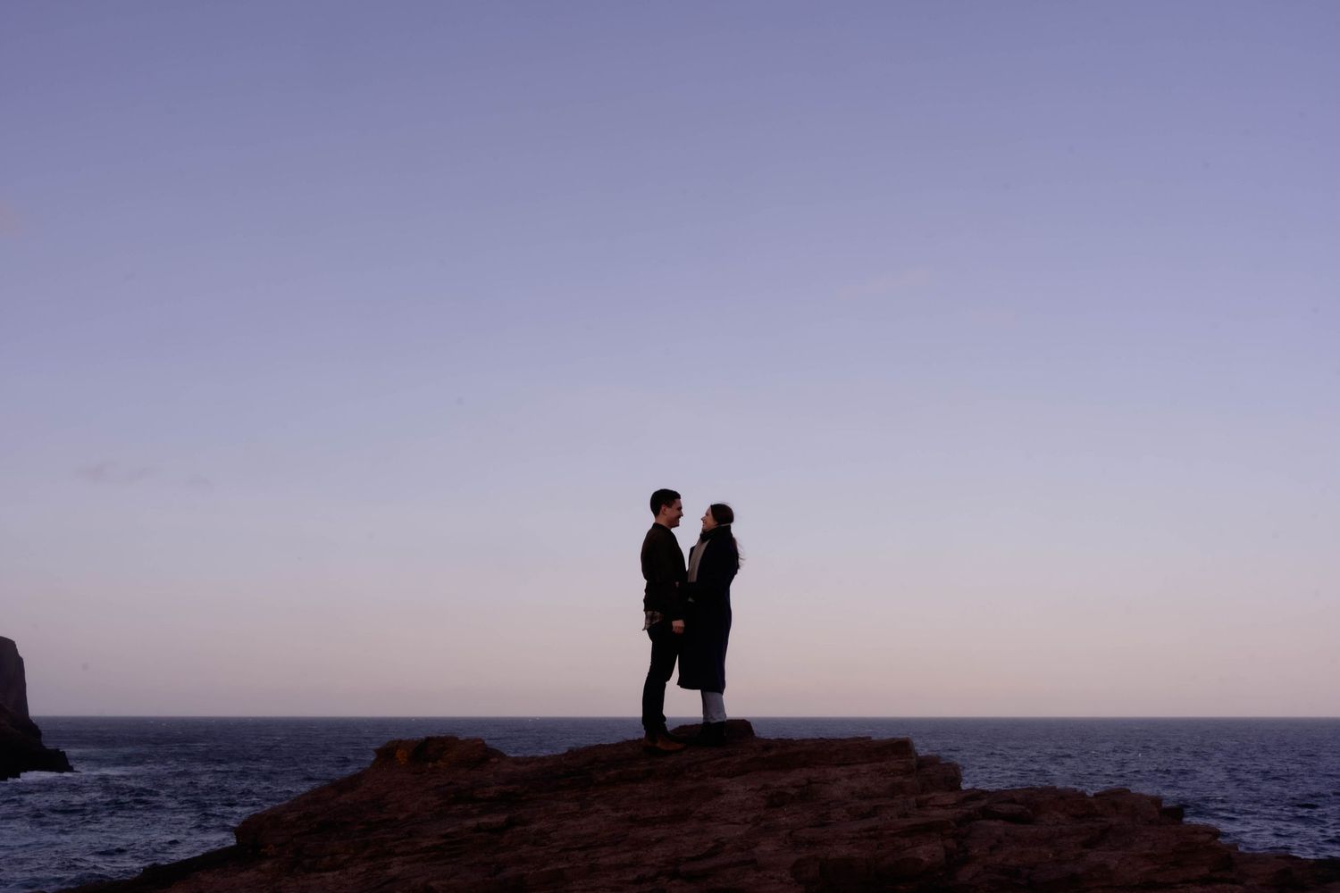 Pre-wedding engagement photo of a couple in silhouette near the Flatrock dwelling, Newfoundland