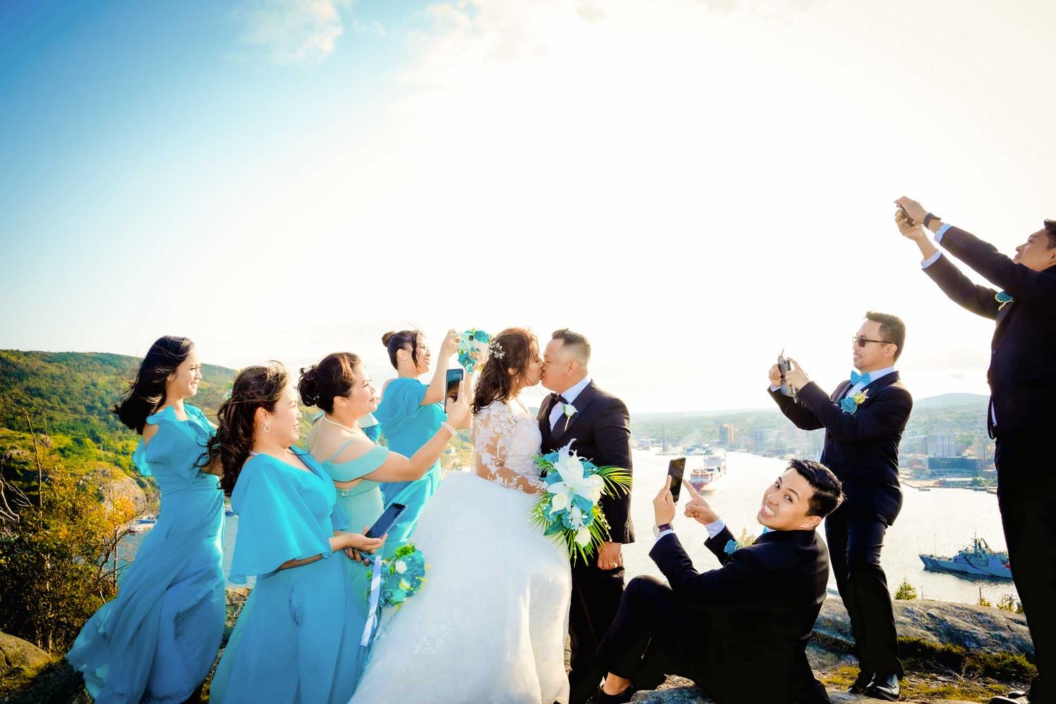 Newlyweds kissing while bridesmaids cheer and snap photos behind them, Newfoundland wedding.