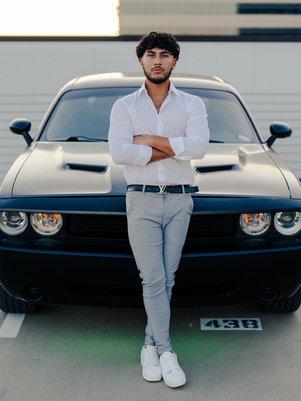 Stylish casual look with white shirt and light pants standing in front of black muscle car.