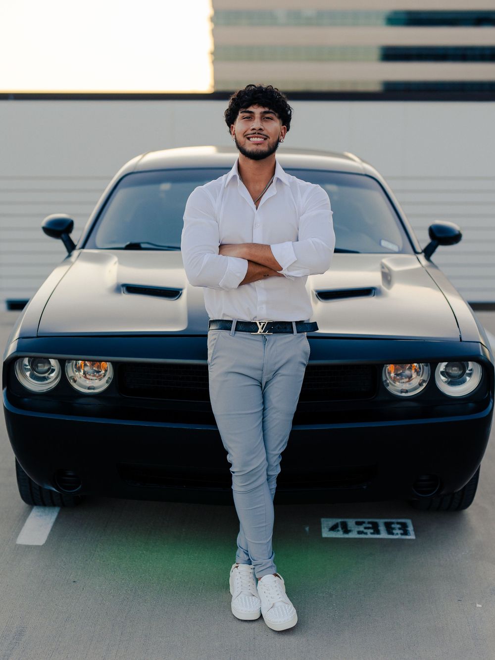 Modern street style featuring crisp white shirt and fitted pants against black sports car backdrop.