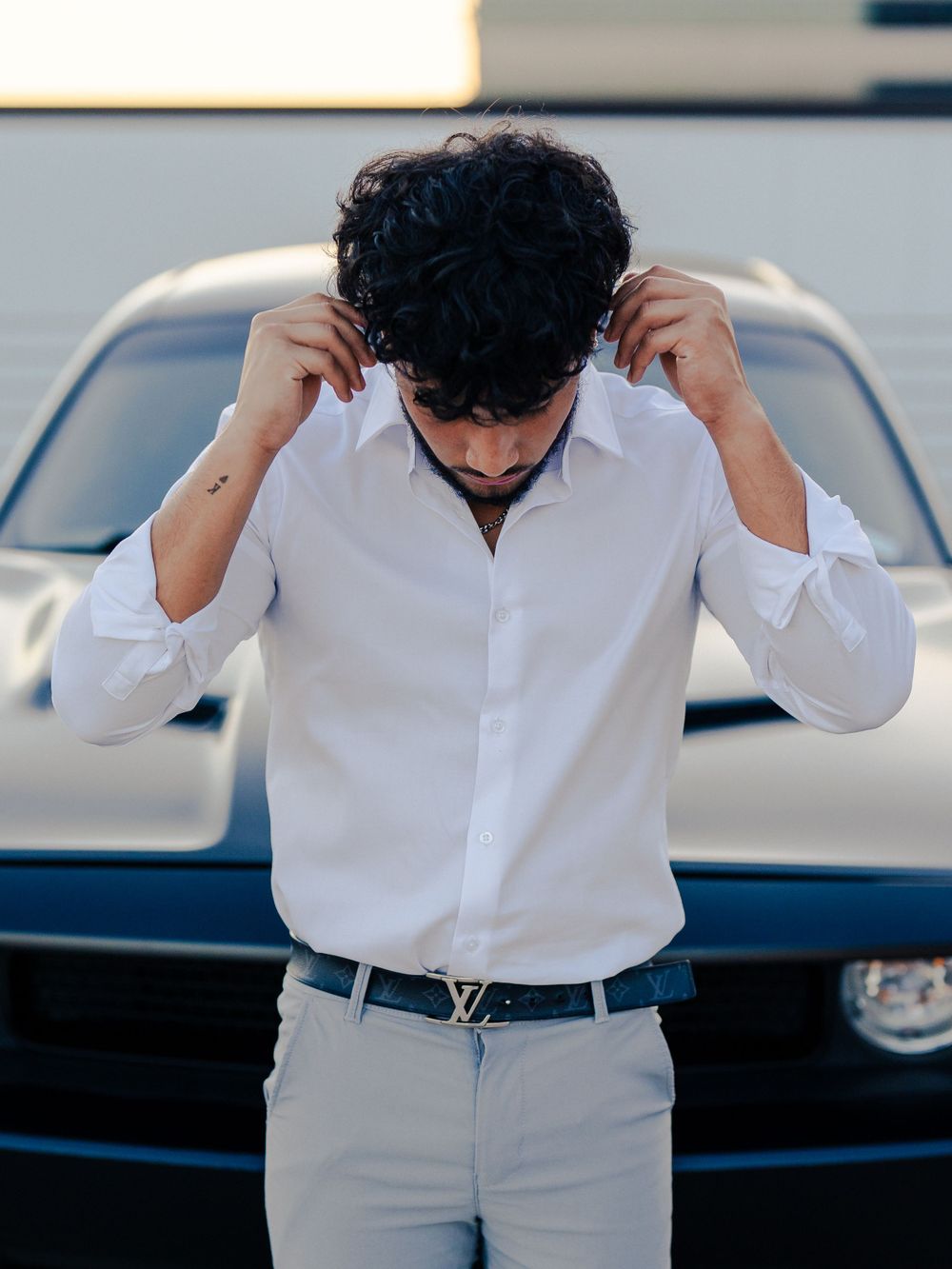 Classic white collared shirt with designer belt styled against sleek black car.