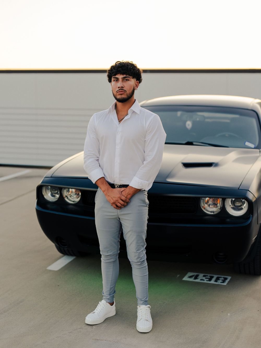 Contemporary casual wear styled with white shirt and light denim against dark sports car.