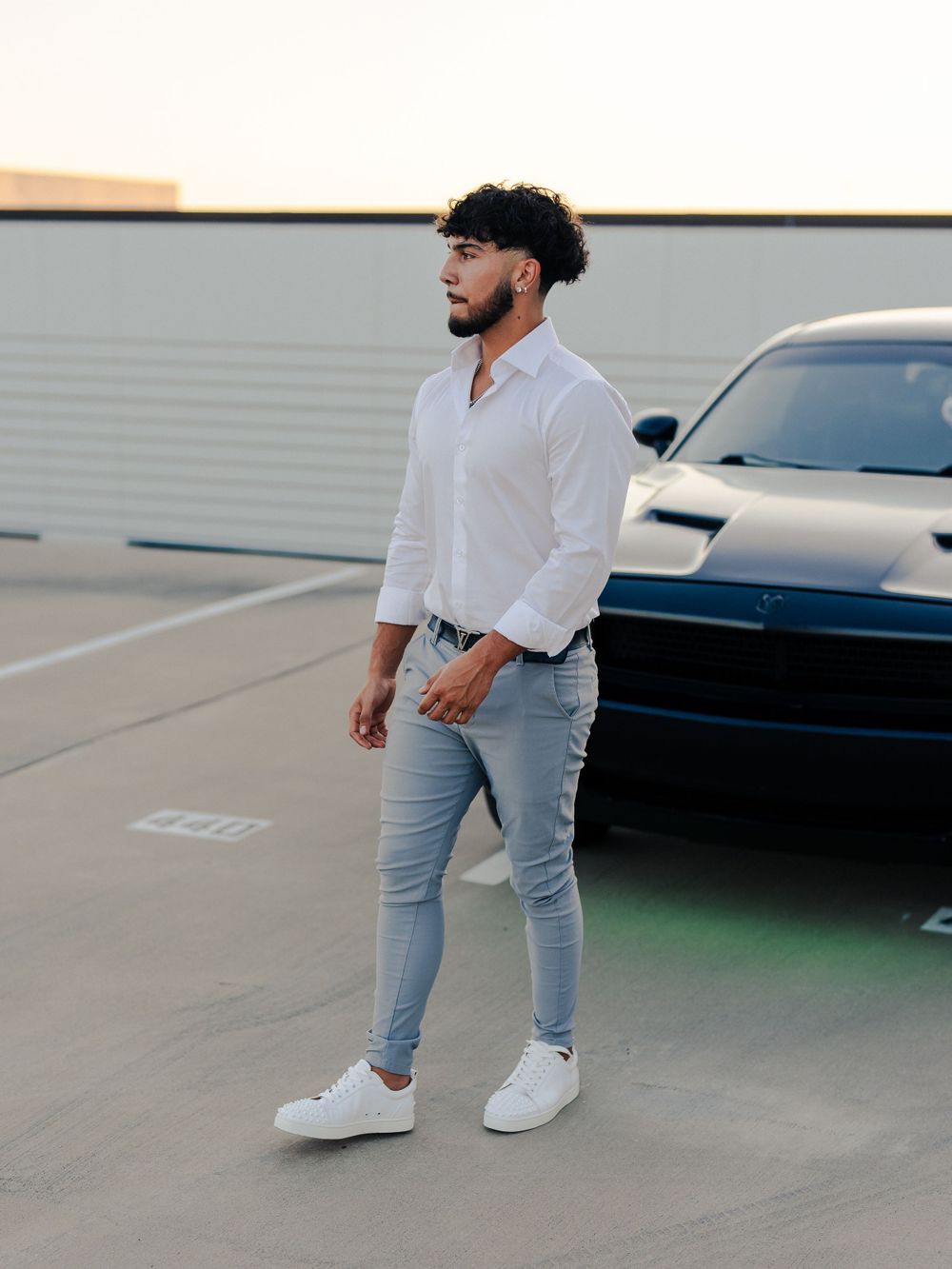 Street style fashion with white button-down and light jeans next to black sports car.