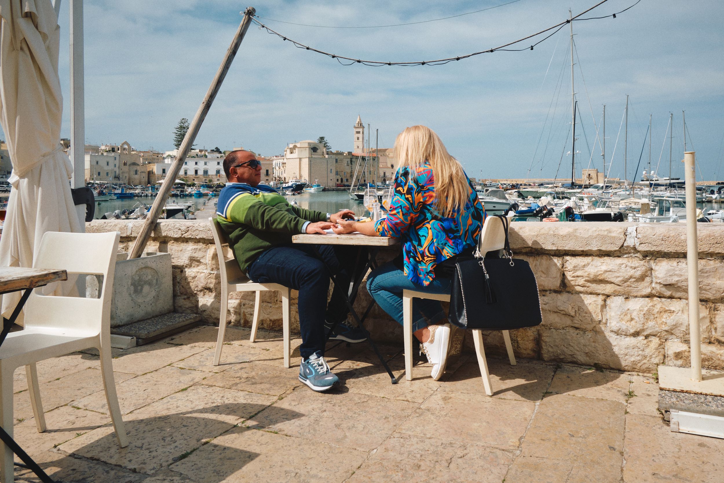Diners enjoying a meal at an outdoor seaside restaurant with marina views.