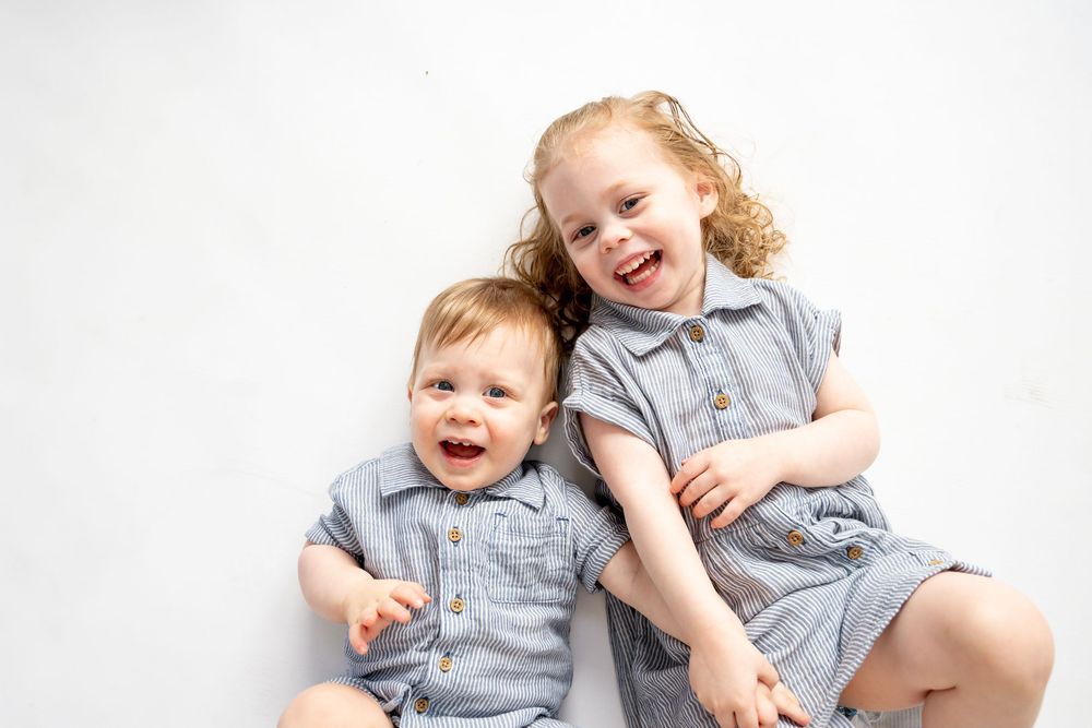 Children wearing matching gray outfits lying on a white background in various playful poses.