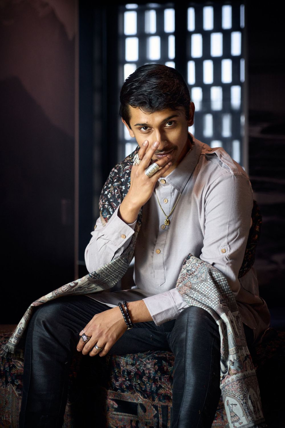 Portrait of person in embroidered shawl and light shirt against geometric window background.