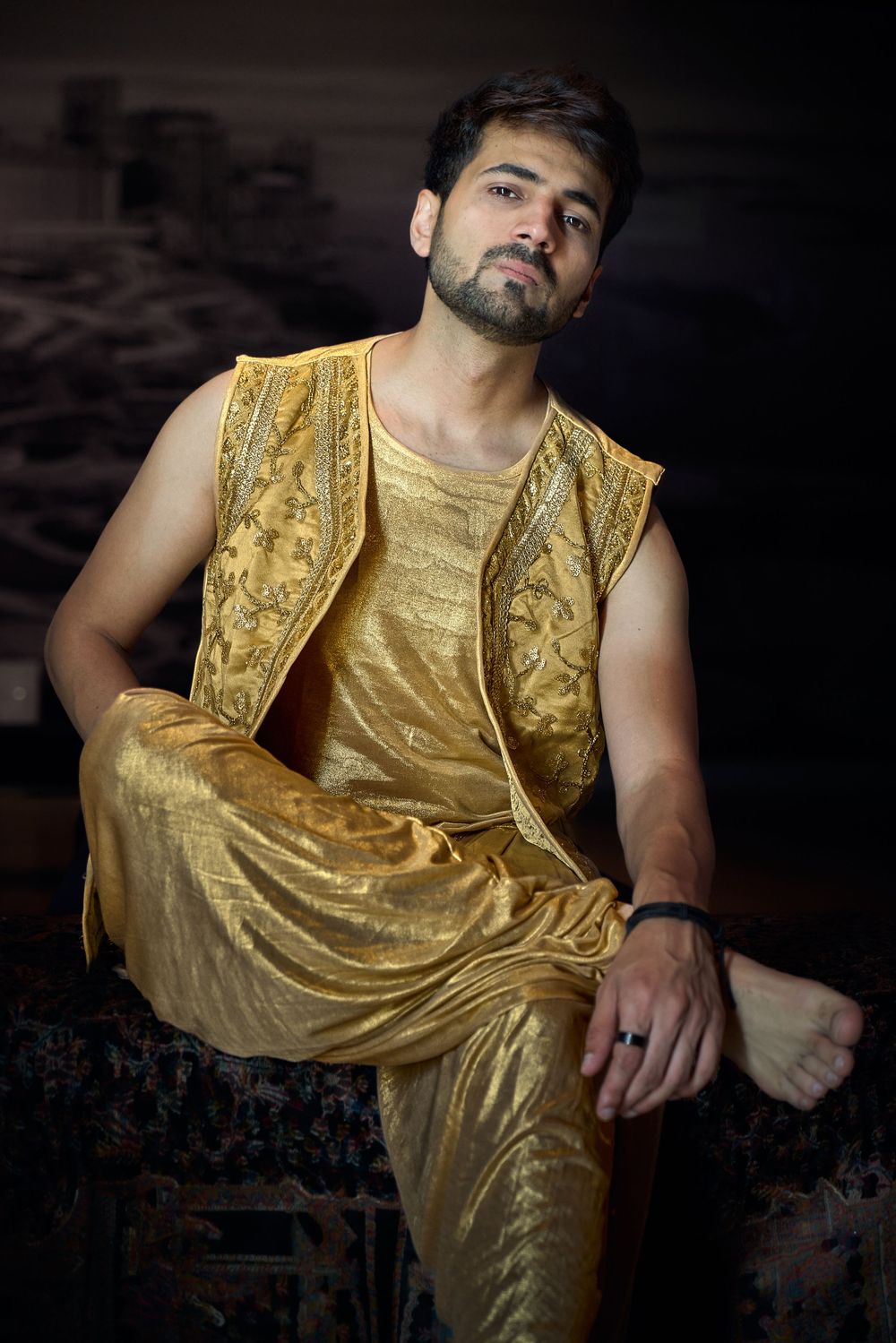 A figure poses in a shimmering gold sleeveless outfit against a dark background in a dramatic fashion photoshoot.