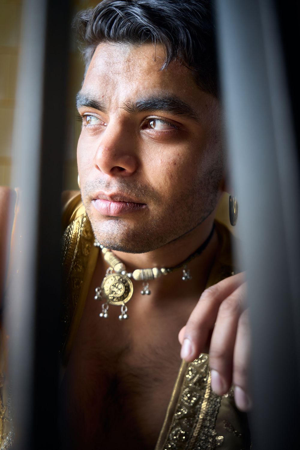 Artistic portrait through bars featuring traditional Indian jewelry and gold accessories.
