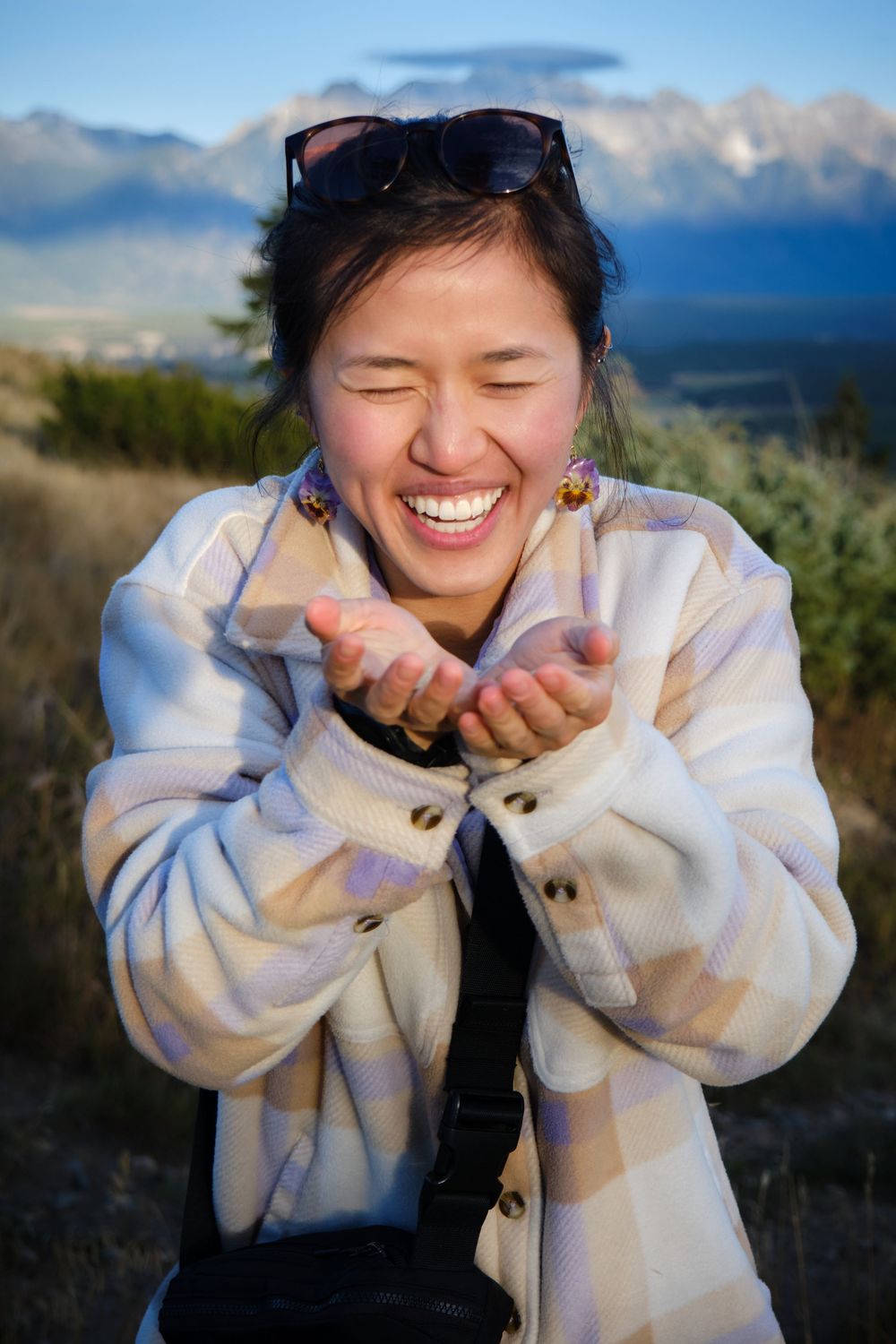 A joyful expression of laughter while wearing a plaid jacket against a scenic mountain backdrop in nature.