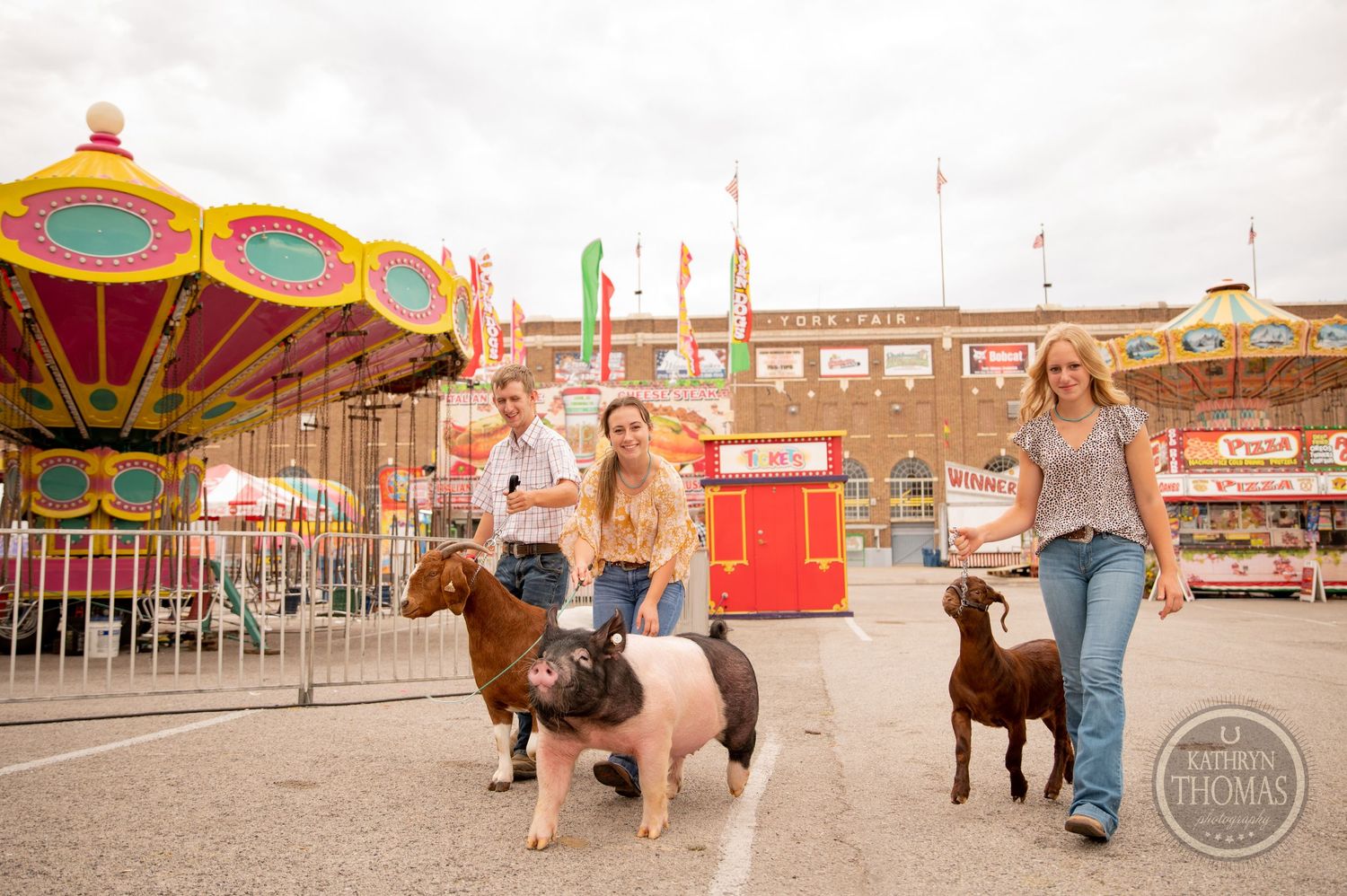 Show pigs and their handlers pose together near carnival rides at the York Fair.