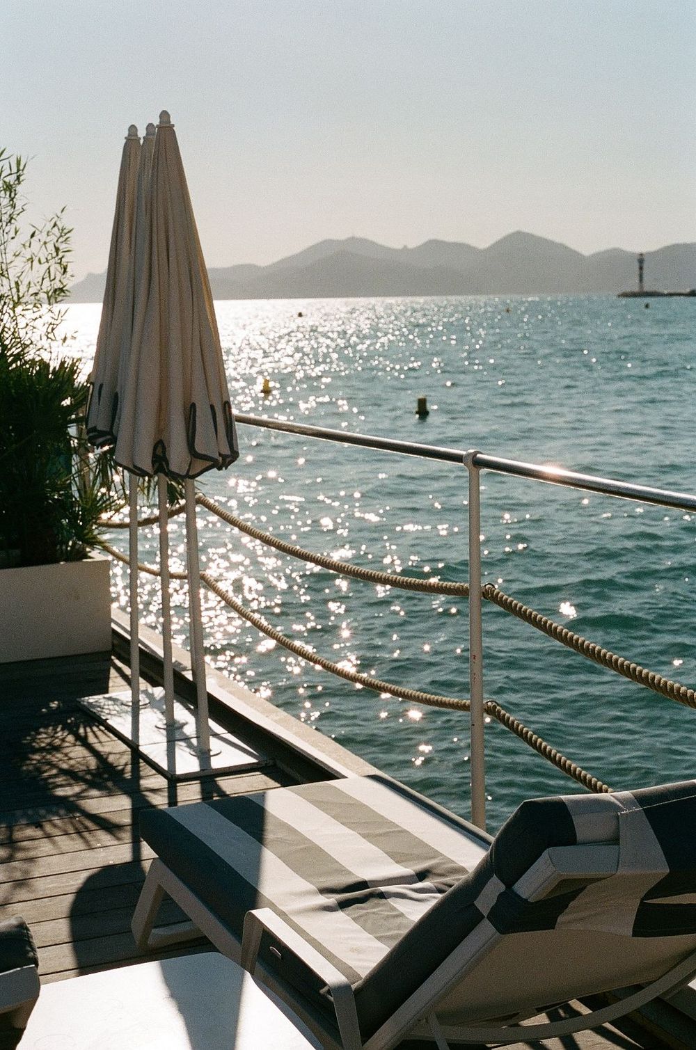 Seaside deck with lounge chairs and folded umbrella overlooking sparkling water and mountain silhouettes at the Carlton hotel in cannes