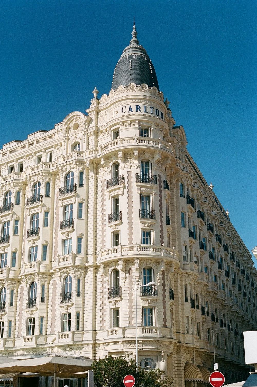 The iconic Carlton Hotel in Cannes features ornate Beaux-Arts architecture against a bright blue sky.
