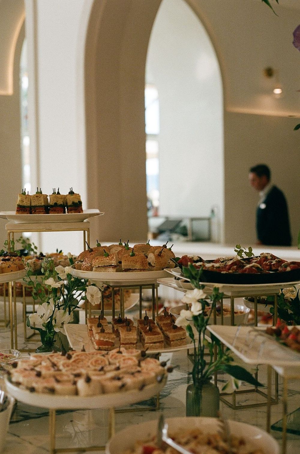 Elegant dessert display with tiered platters of pastries and treats adorned with greenery at an event.