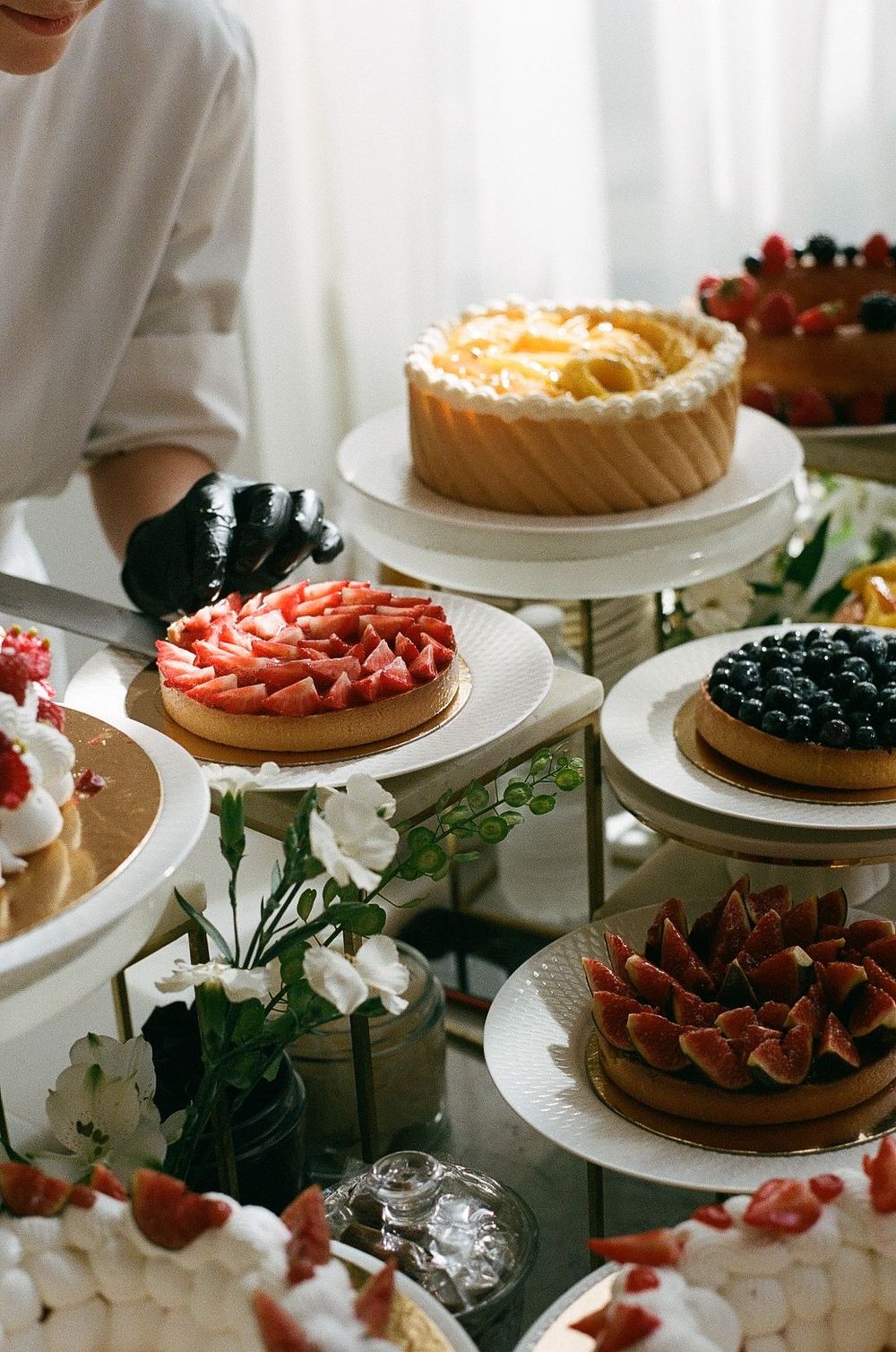 Colorful array of fruit tarts and cakes displayed on white cake stands with floral decorations at the Carlton hotel in cannes