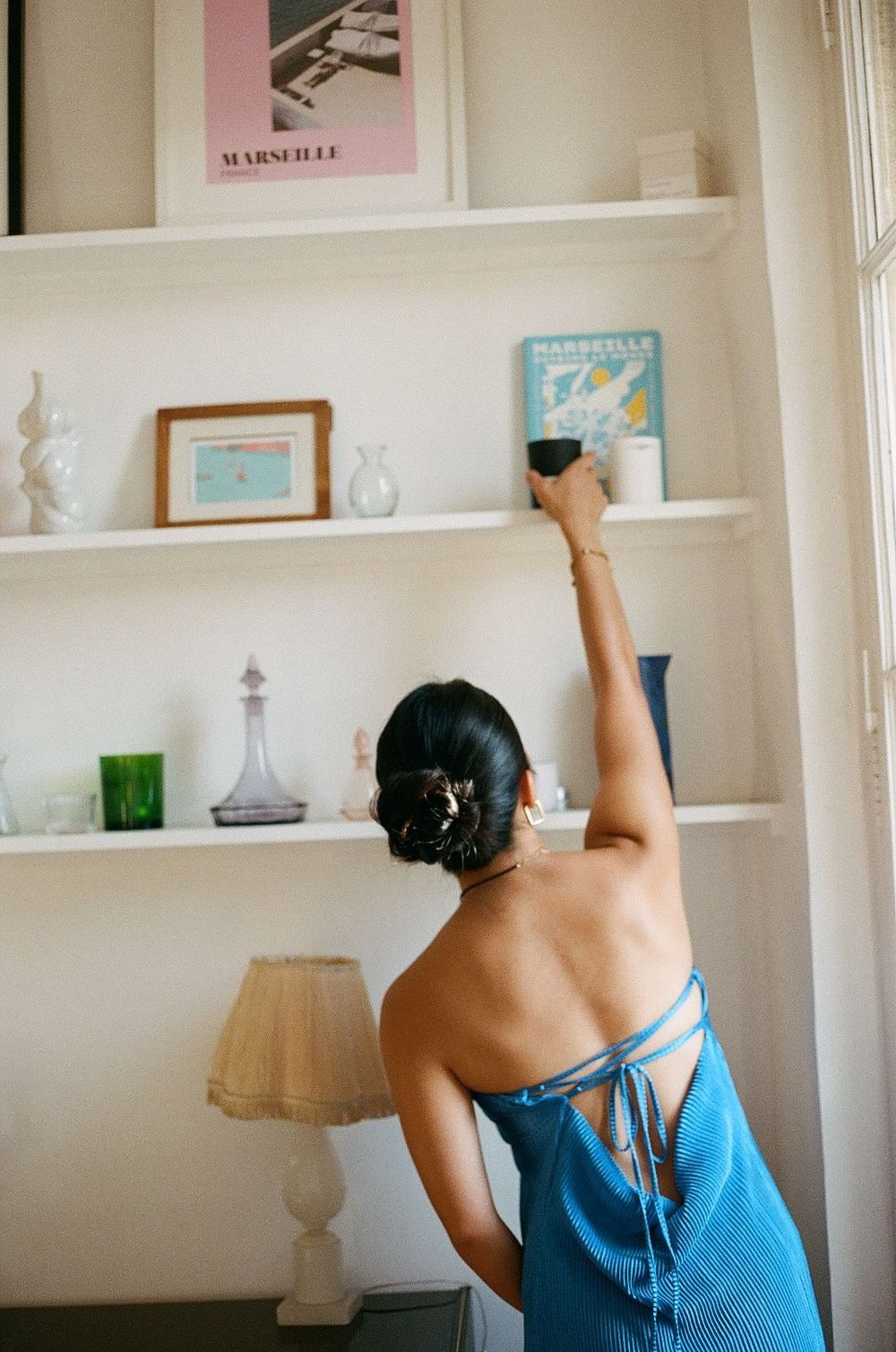Someone reaching up to arrange items on white built-in shelves displaying art and decorative objects.