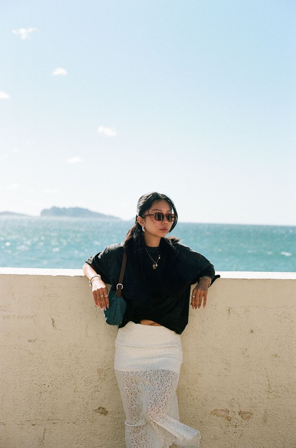Stylish beachside portrait featuring sunglasses and white lace skirt against ocean backdrop in Marseille taken on film