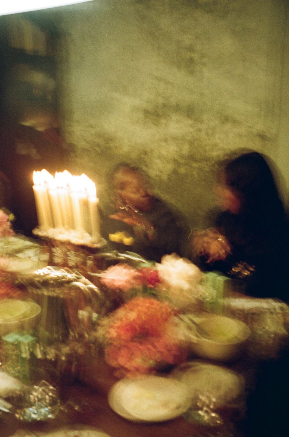 Moody candlelit dinner table setting with blurred figures in warm vintage tones.