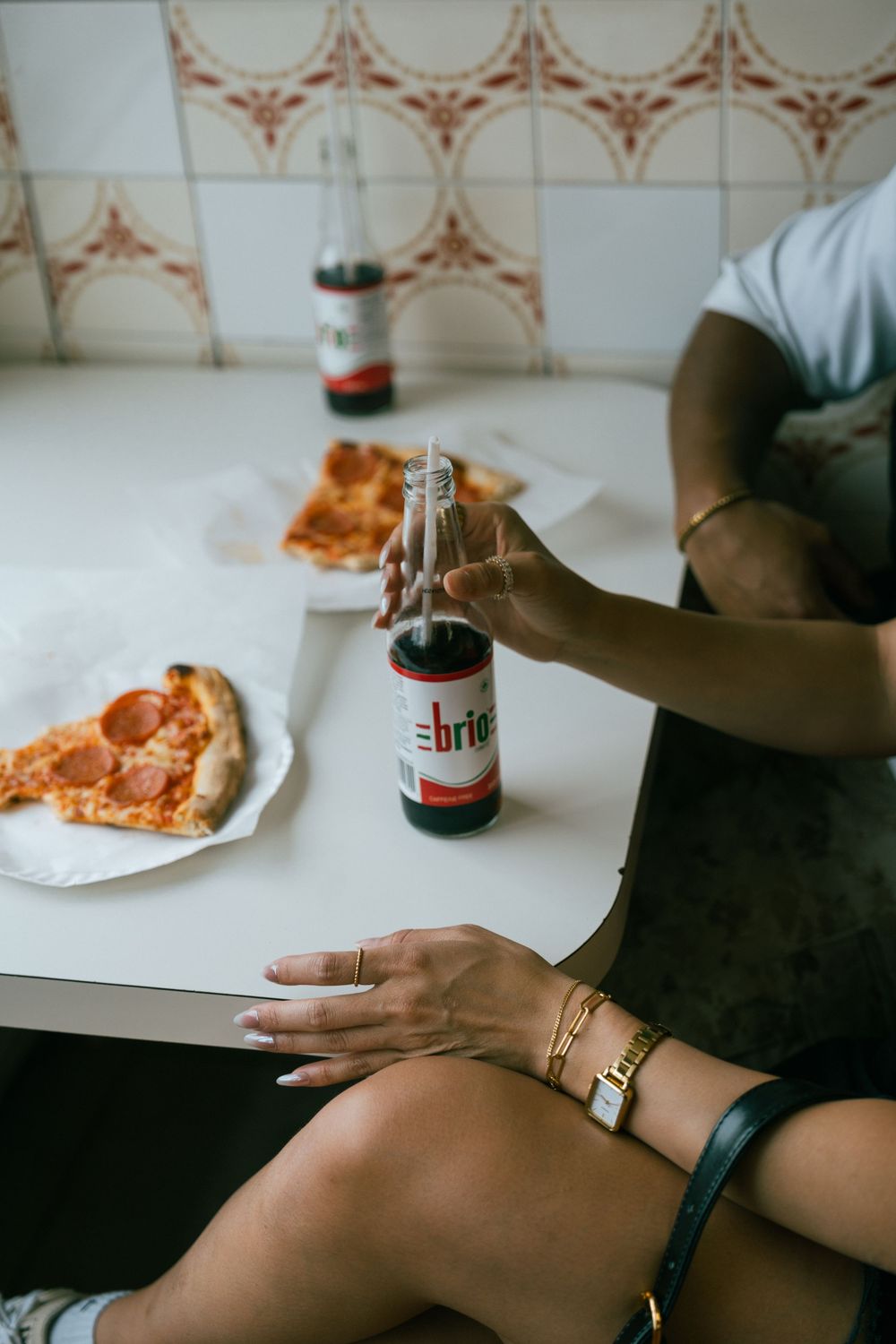 Close-up of hands holding a Sprite bottle with pizza slices on white plates in background.