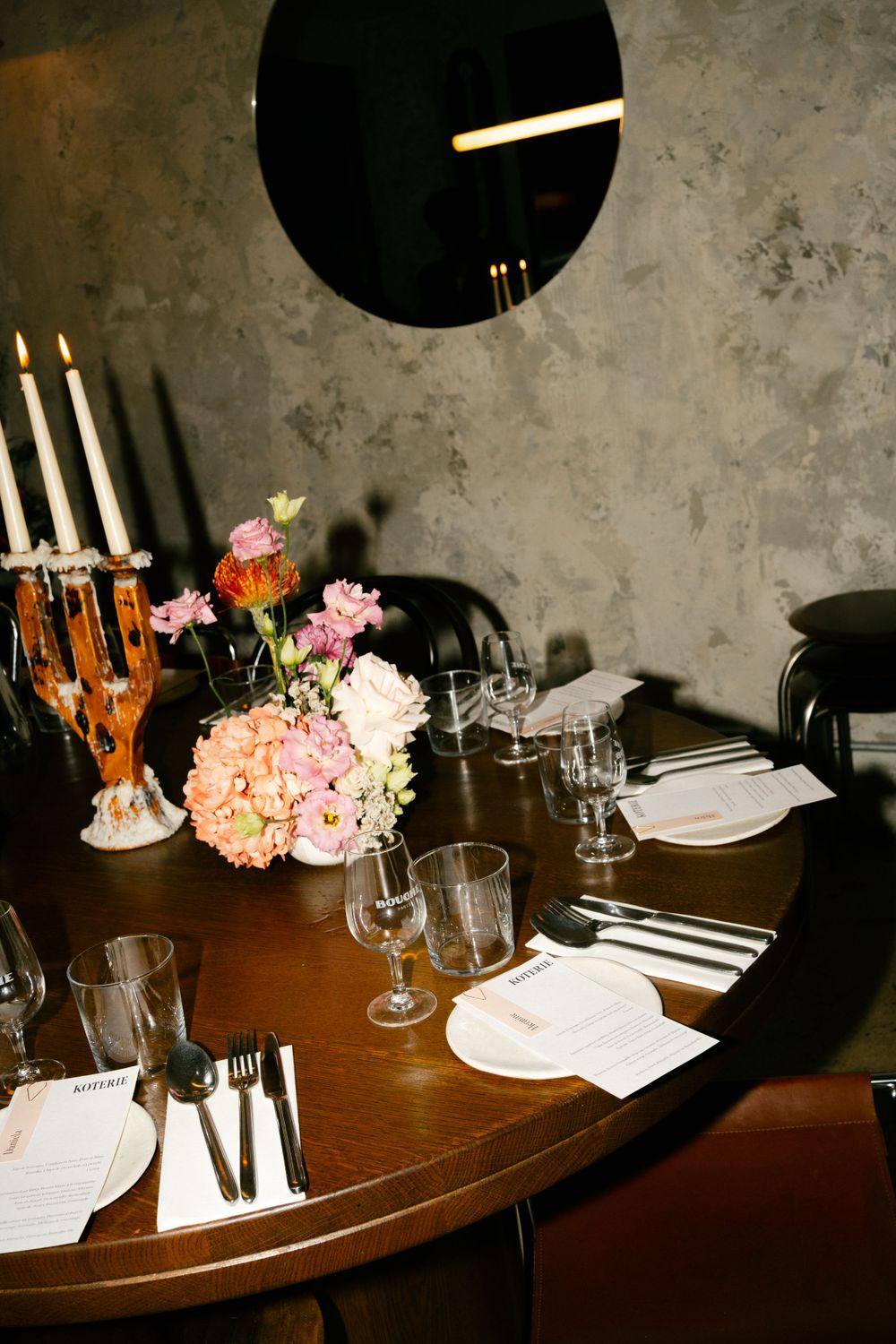 Elegant table setting with pink floral centerpiece, candles and wine glasses in a moody dining room.