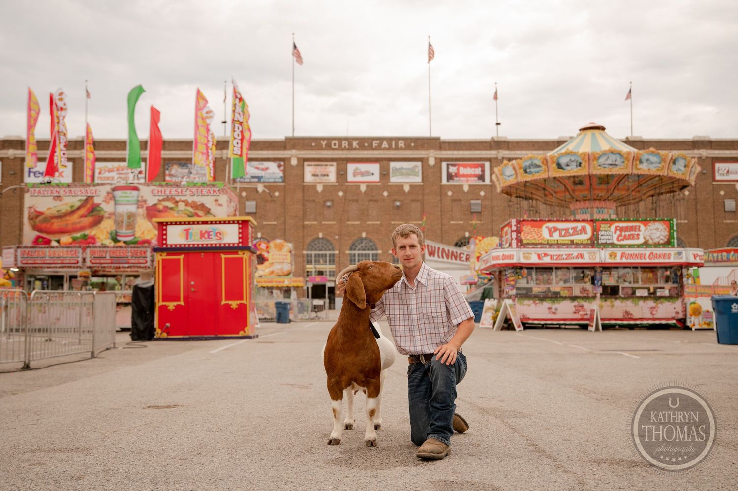 A show goat and handler pose in front of the York Fair building and carnival grounds.