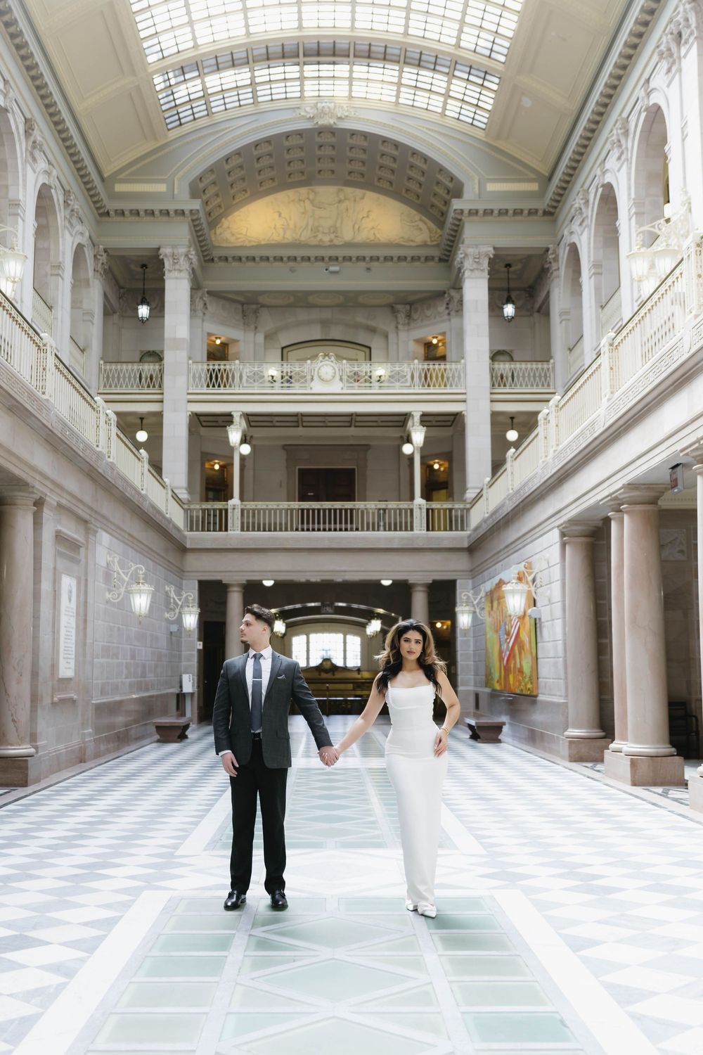 A couple walks through an elegant marble hall with checkered floors and classical columns.