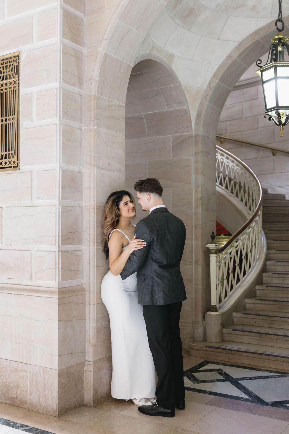 A romantic moment captured in an elegant marble hallway with arched columns and a grand staircase.