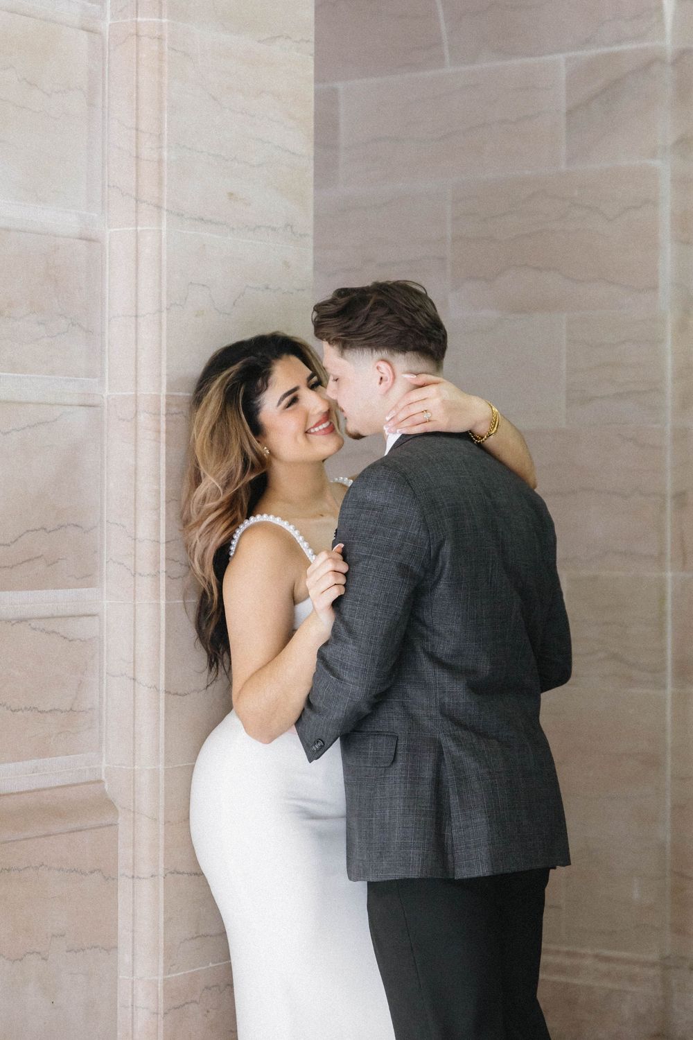 Joyful wedding couple embraces in an elegant marble hallway with natural lighting.