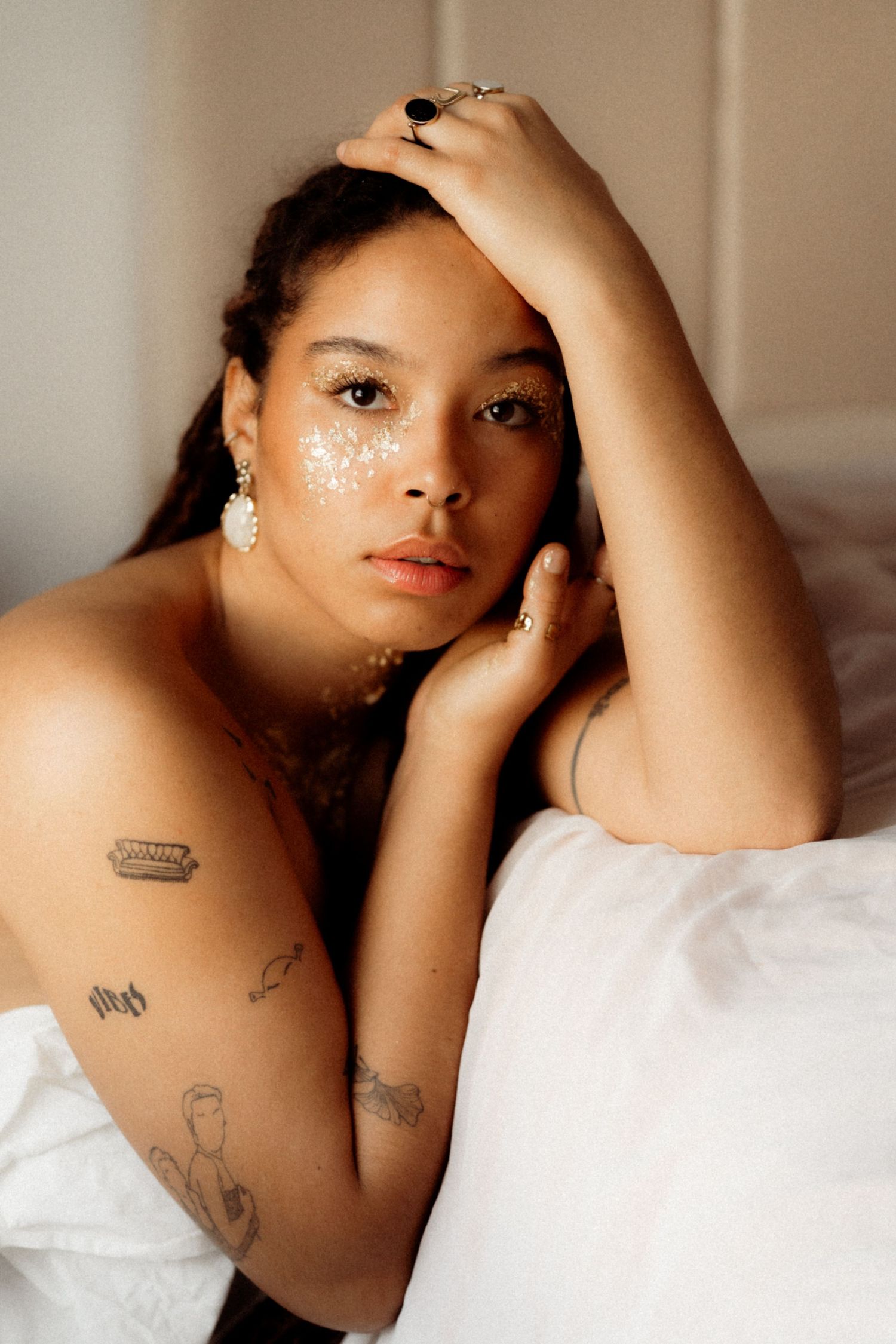 Artistic portrait with white face paint details and visible tattoos against white background.