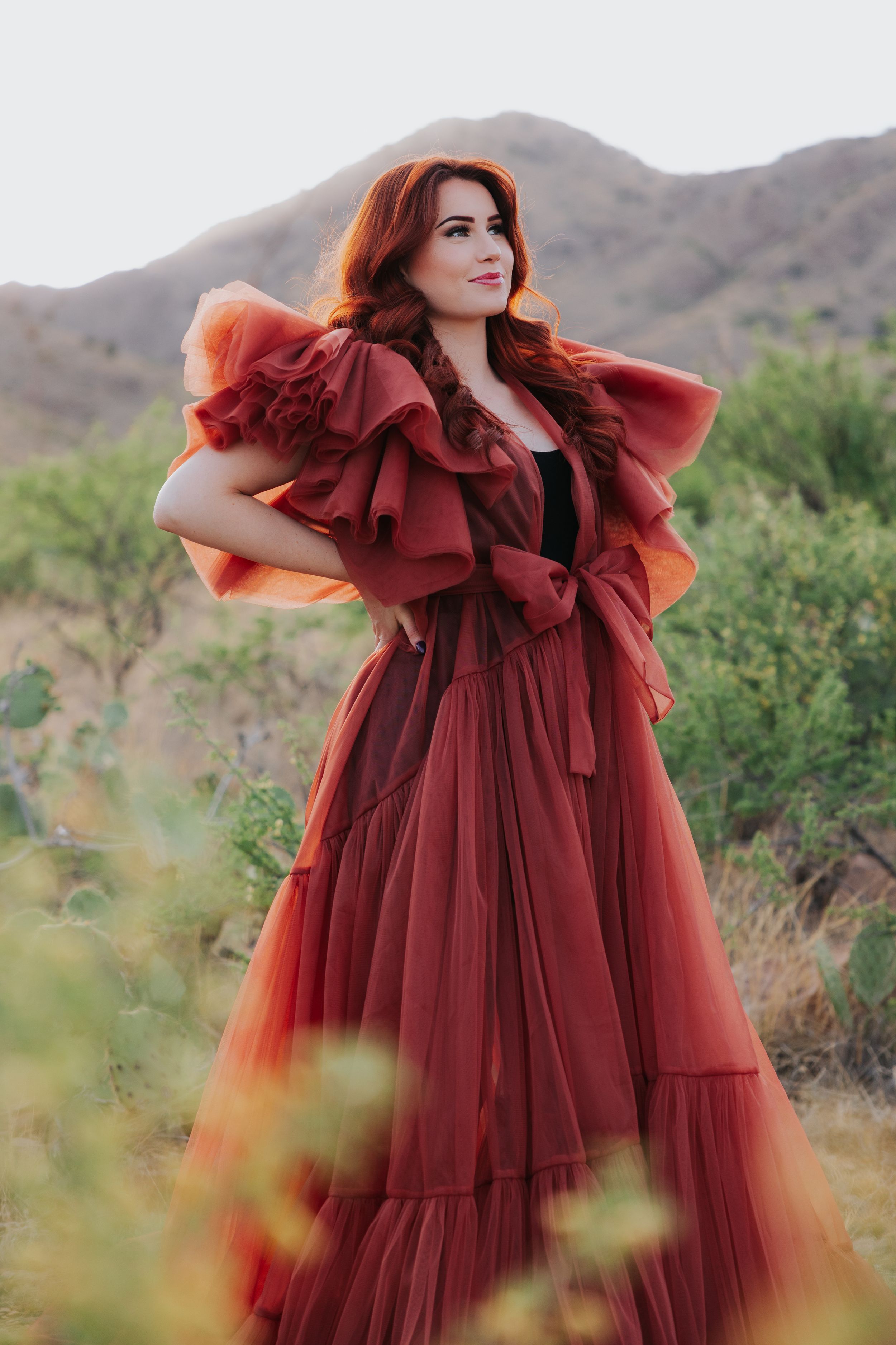 A romantic burgundy tulle gown with ruffled details photographed against desert mountains.