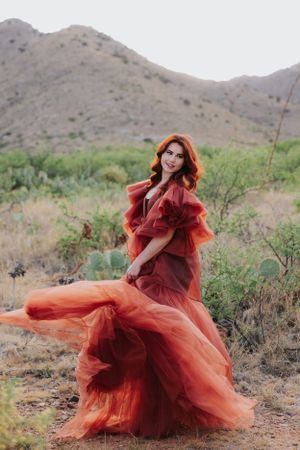 Flowing red tulle gown billows dramatically against desert mountain landscape in artistic fashion photoshoot.